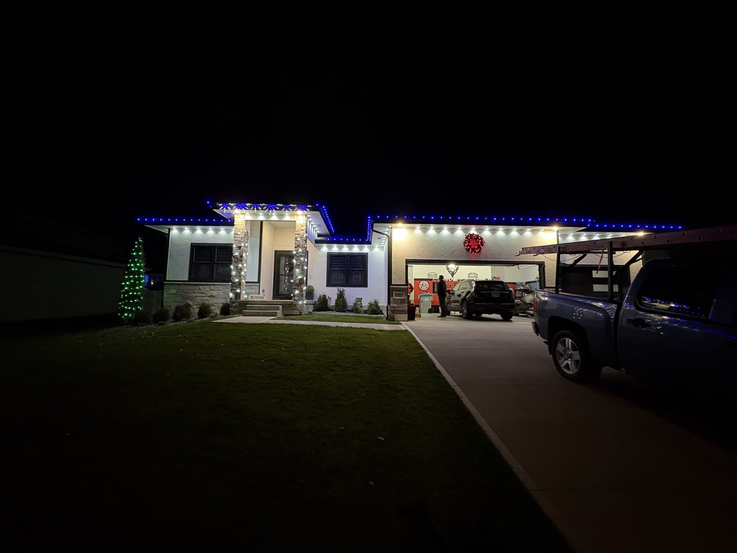 Modern ranch home with blue and warm white roofline lights and a lit evergreen